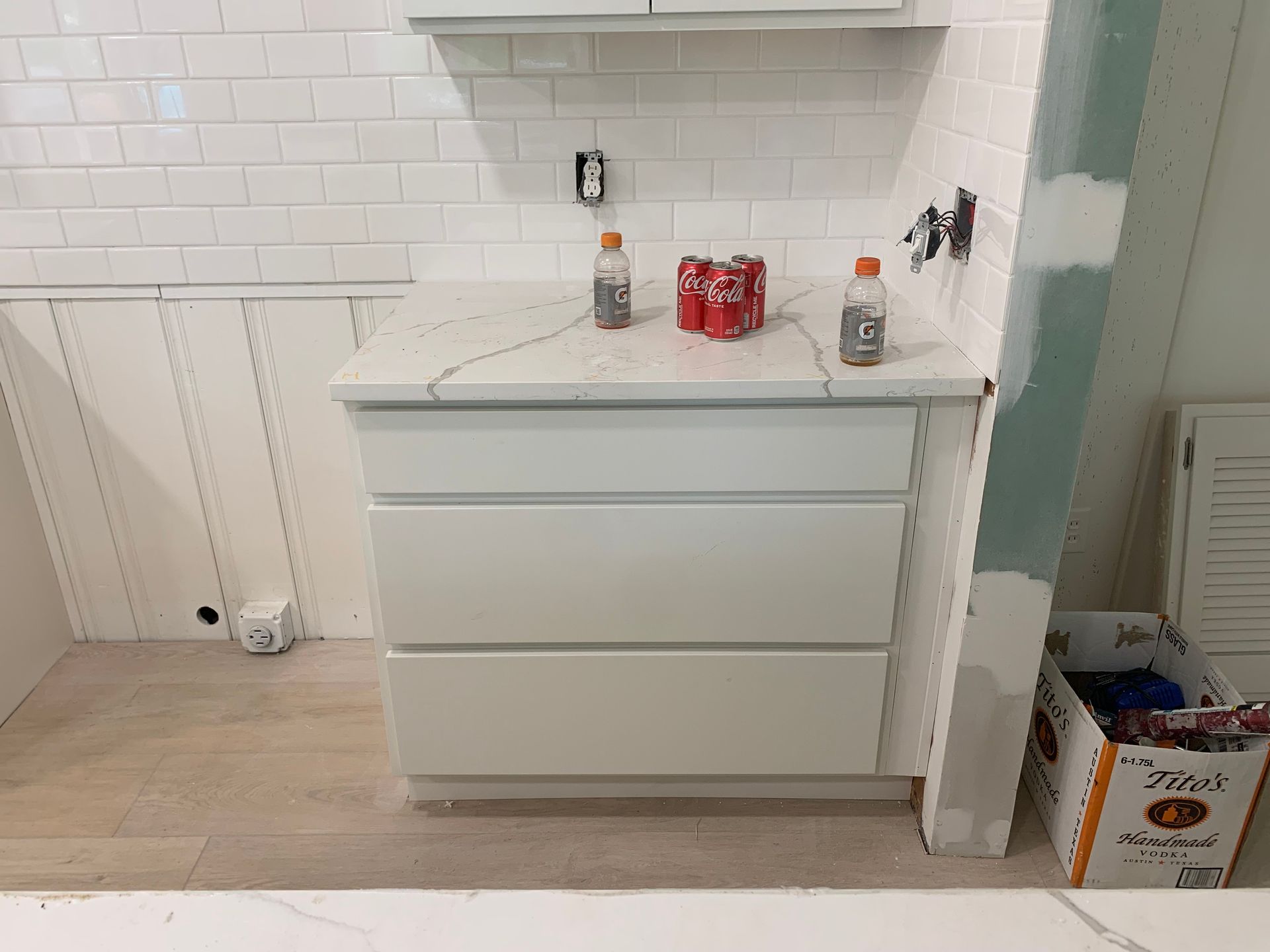 Empty white kitchen with lower cabinets, tiled backsplash, and items on the countertop.