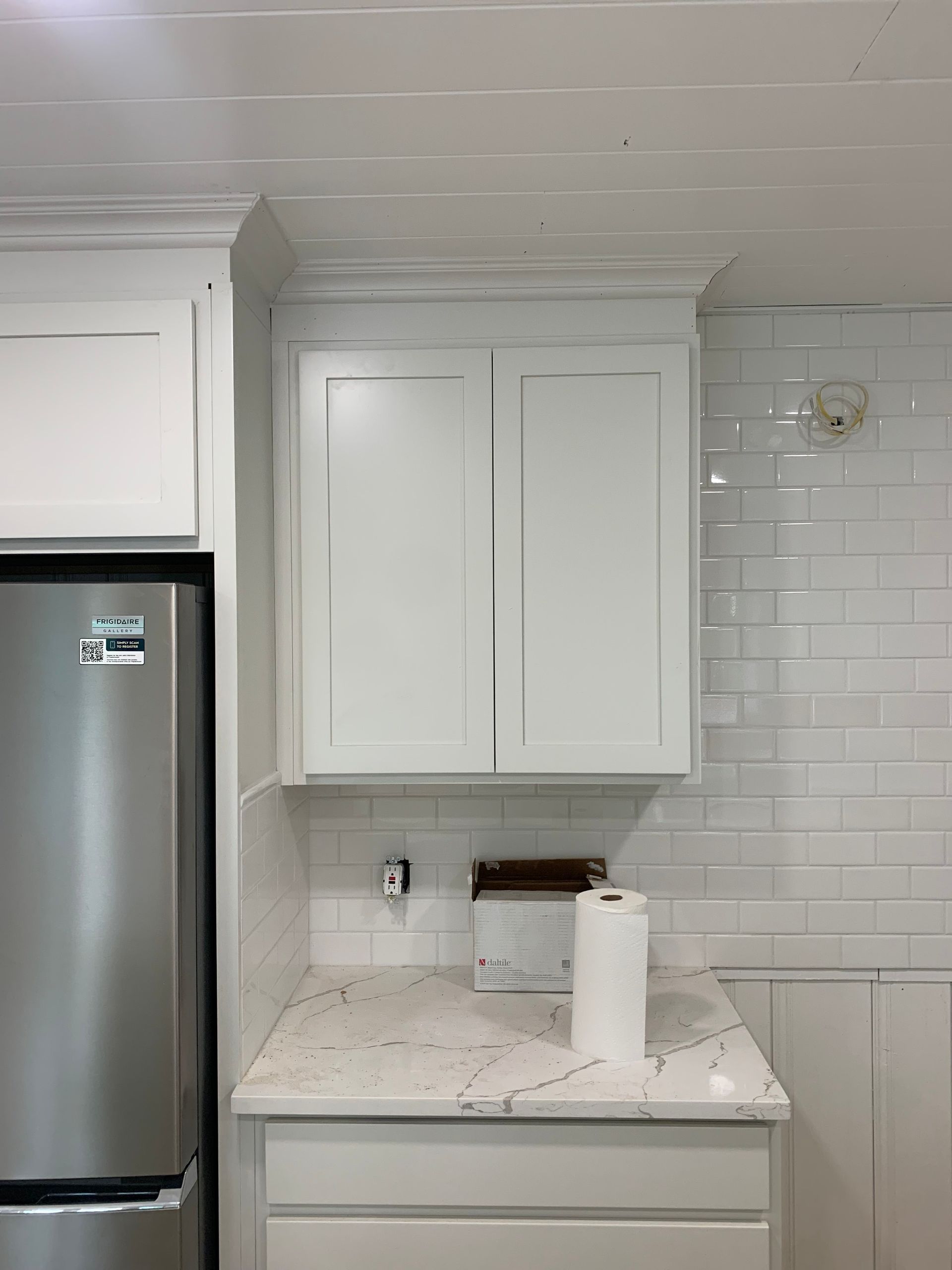 White kitchen nook with cabinets, stainless fridge, marble countertop, and subway tile backsplash