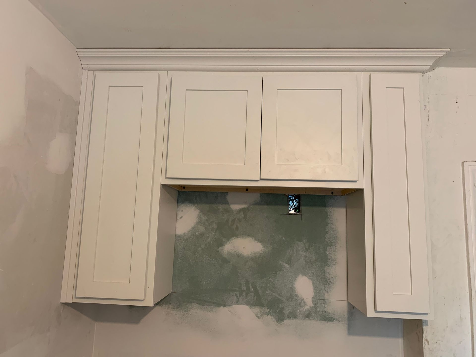 White kitchen cabinets over a framed opening with unfinished wall beneath.