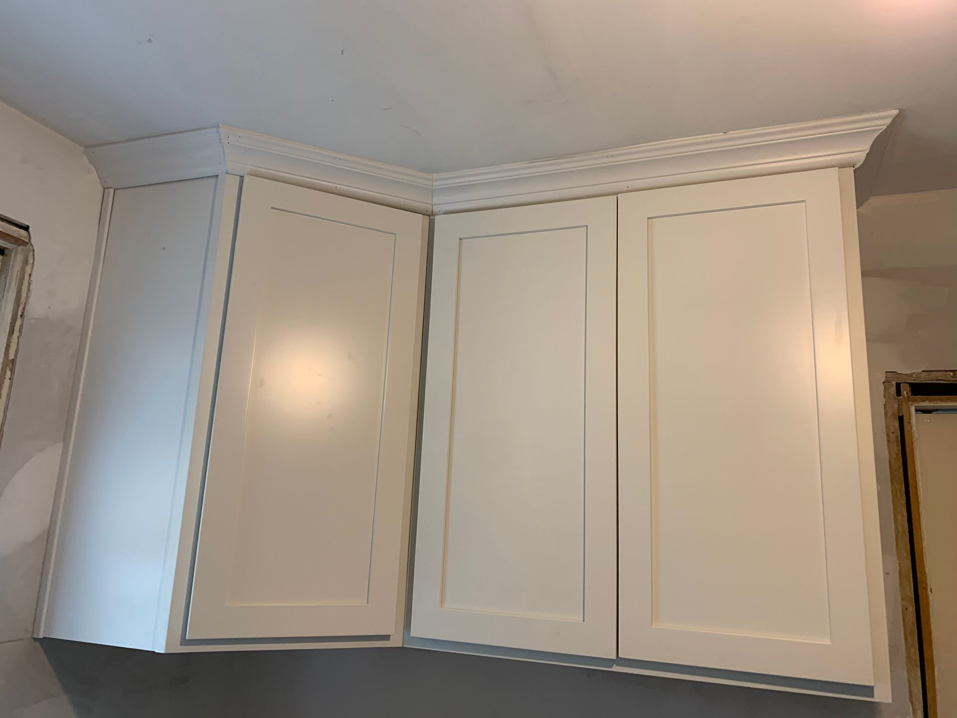 White kitchen wall cabinets above a counter, with crown molding and a mirrored panel on the right