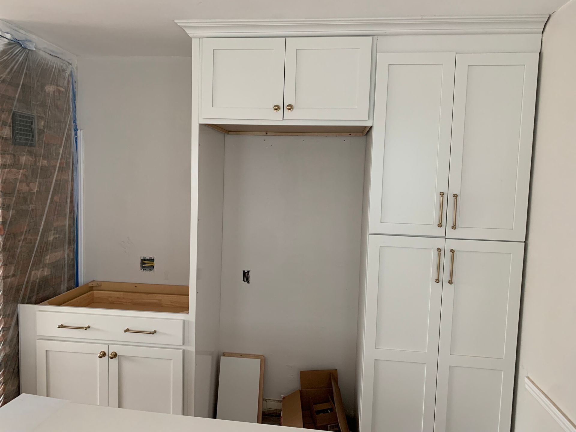 Built-in white cabinets and drawers in a small room, with a doorway and plastic-covered item on the left.