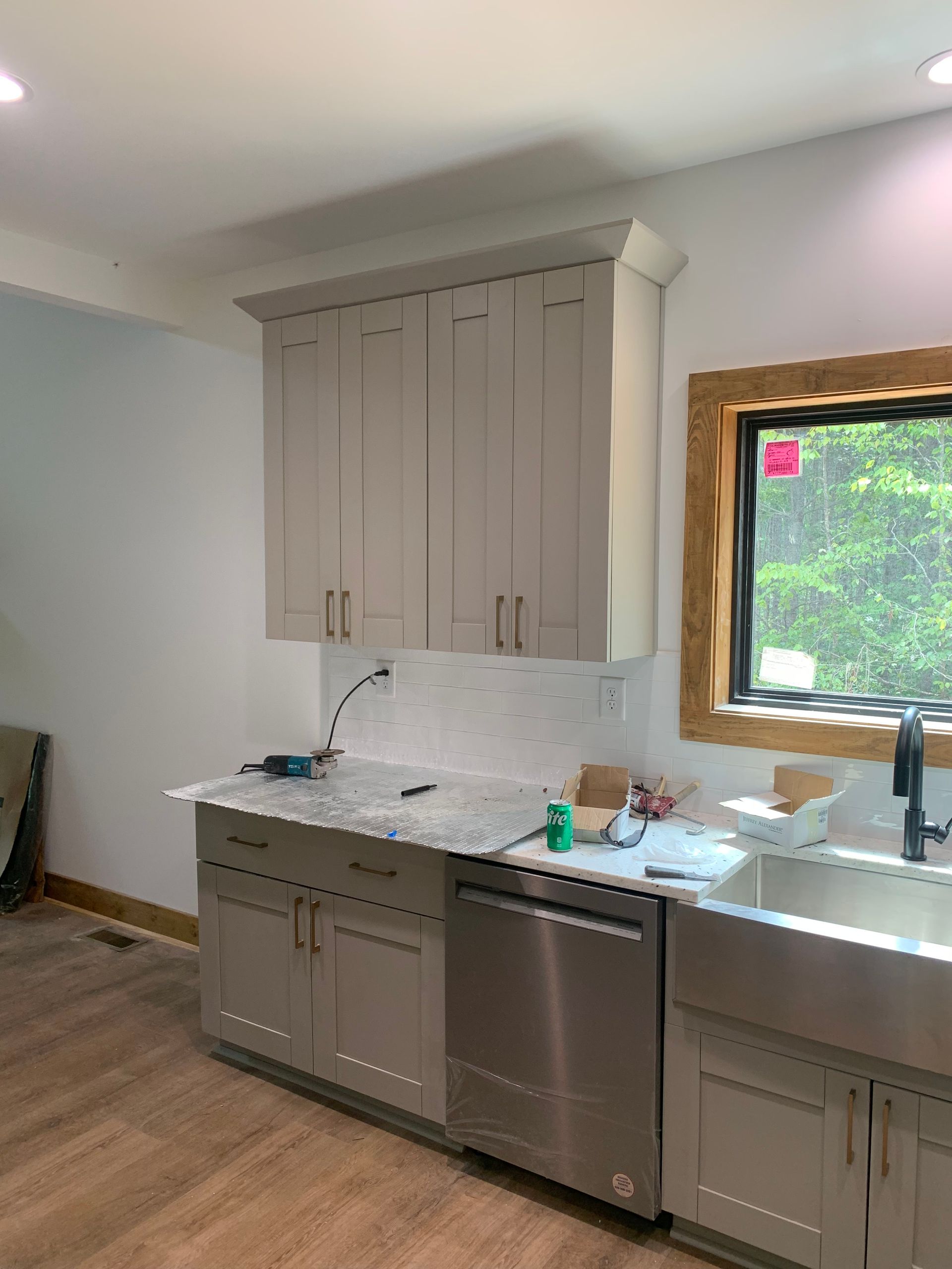 Modern kitchen with gray cabinets, stainless dishwasher, white marble countertop, and window over sink
