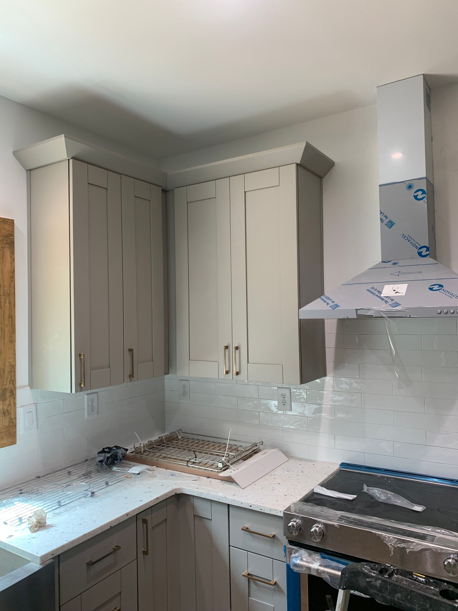 Small kitchen with white cabinets, tiled backsplash, countertop clutter, and a stainless steel stove with hood.