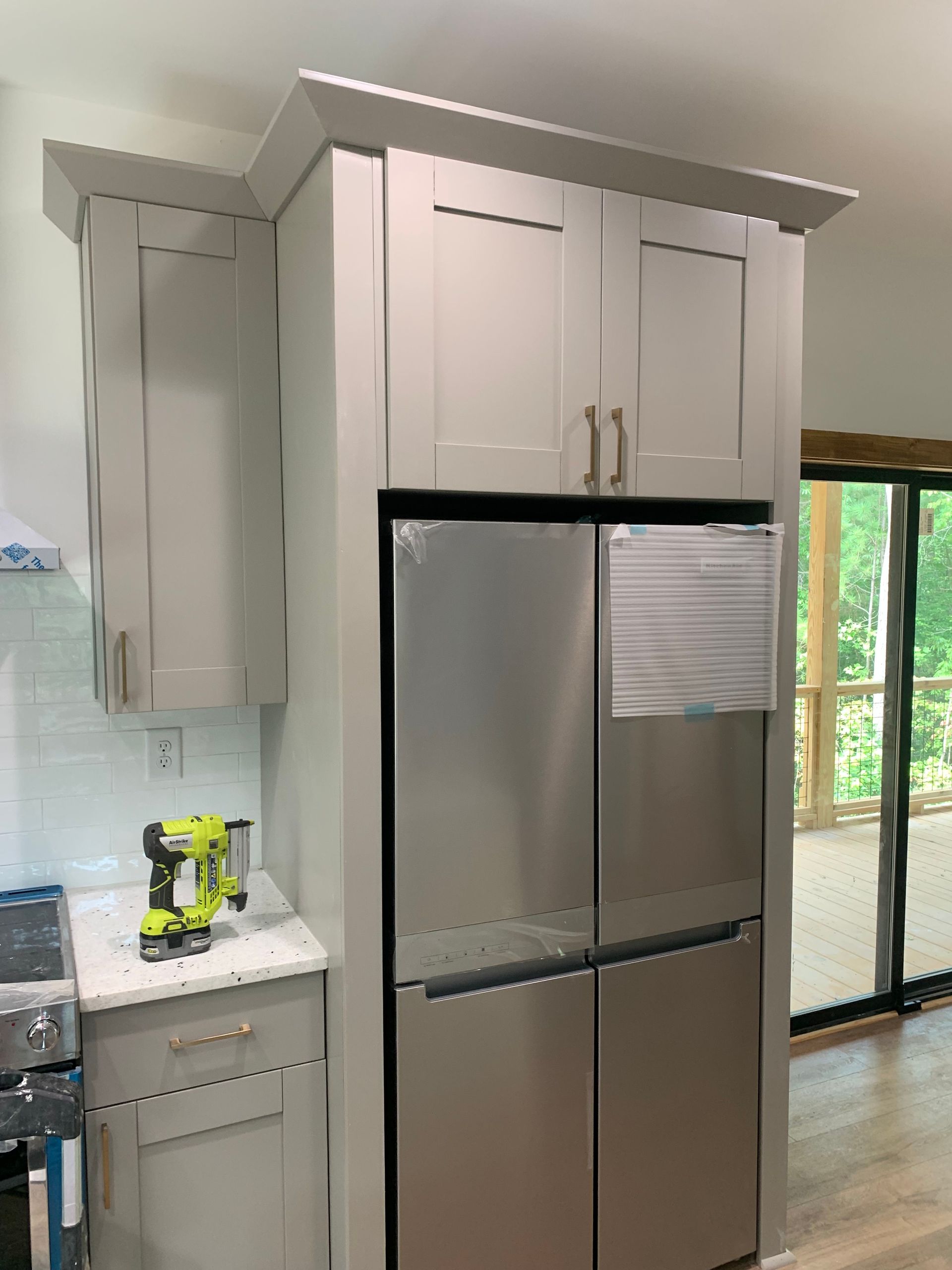 Kitchen with stainless steel refrigerator, light cabinets, and a window by a white countertop.
