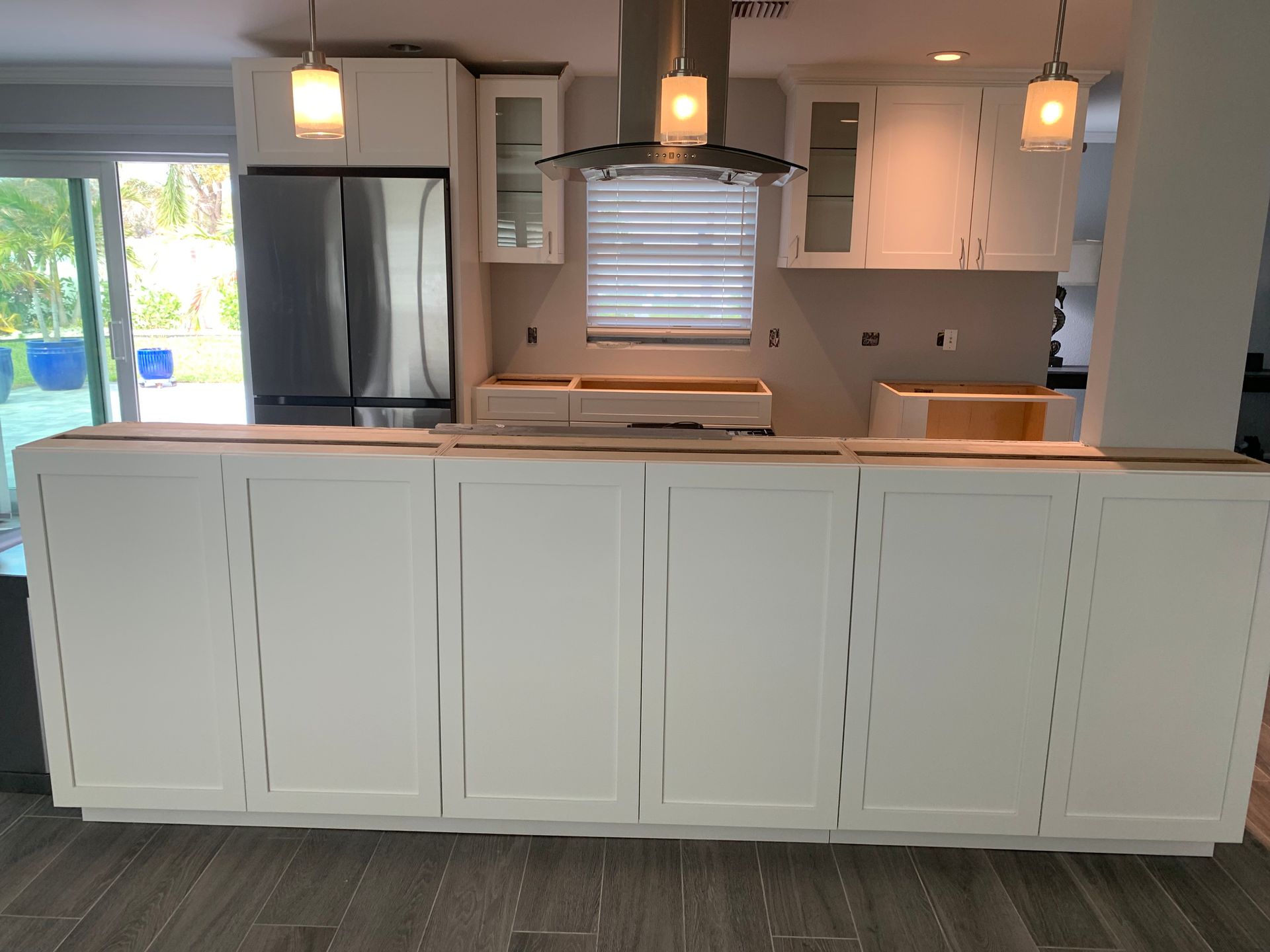 White kitchen with large island, pendant lights, stainless fridge, and a window over the sink.