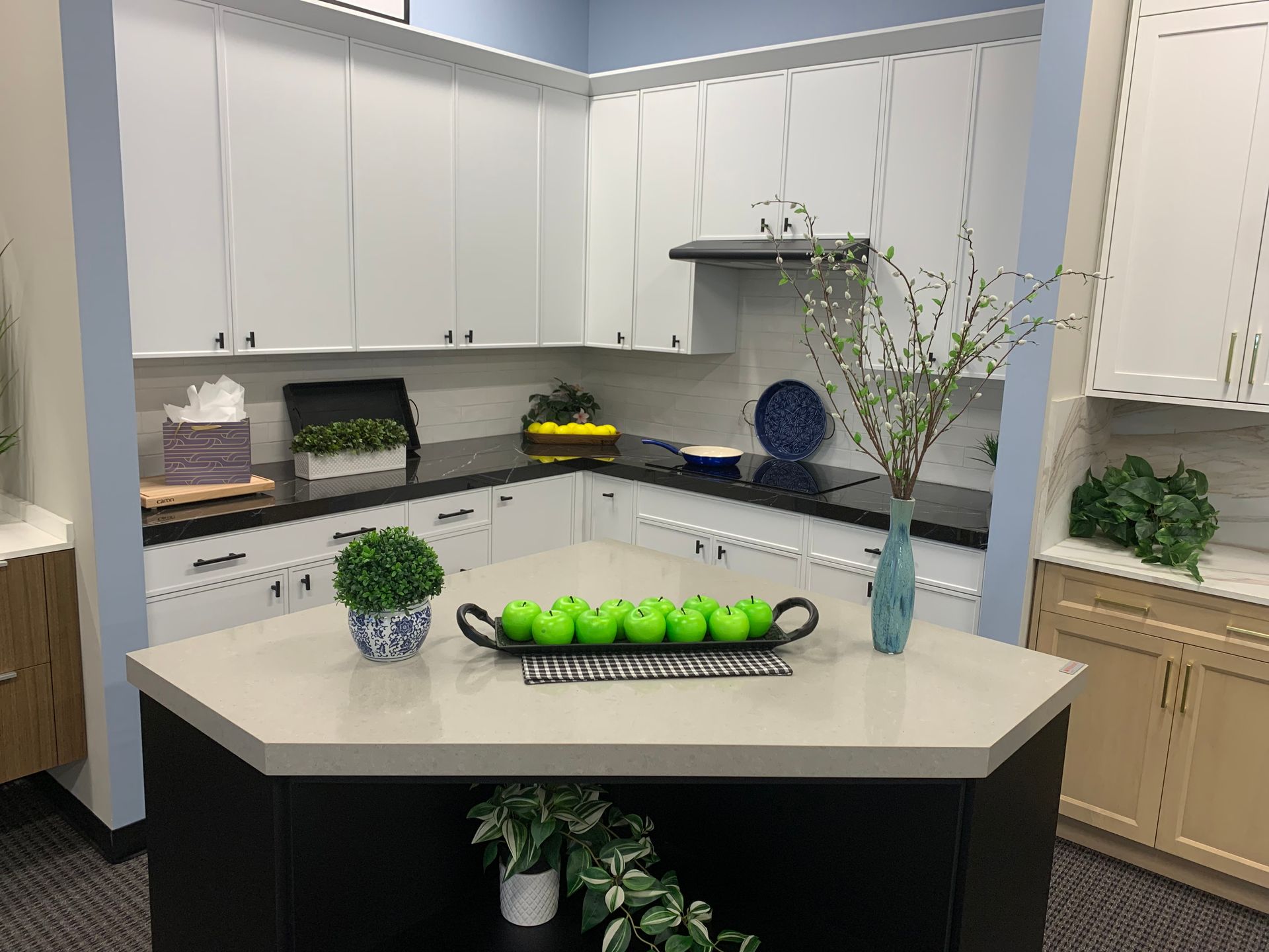 Modern white kitchen with island, fruit bowl, potted plants, and decorative vases