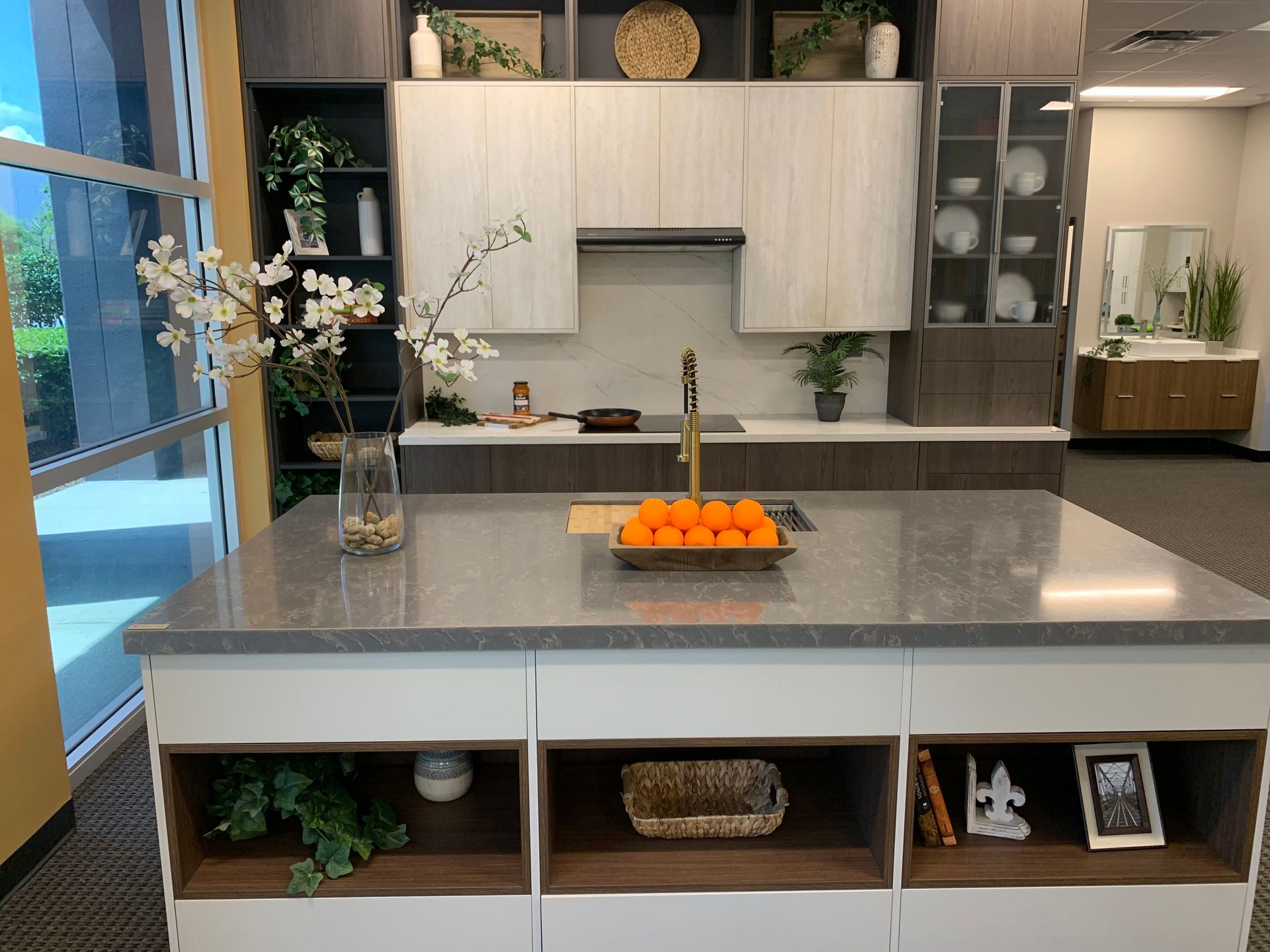 Modern kitchen interior with gray island, fruit bowl, white cabinets, and open shelves by a large window