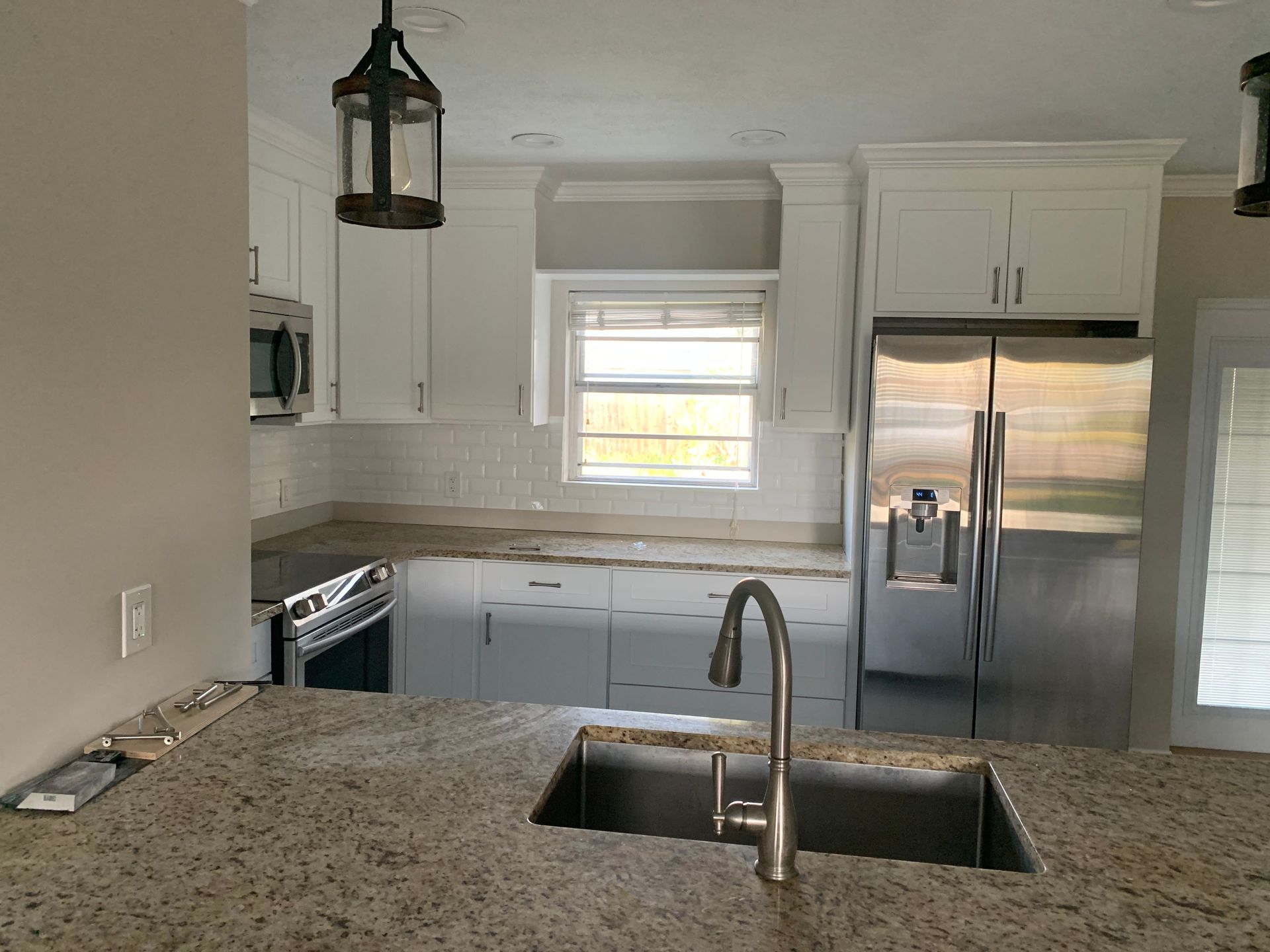 Bright kitchen with white cabinets, stainless steel fridge, and a granite island with sink and faucet.