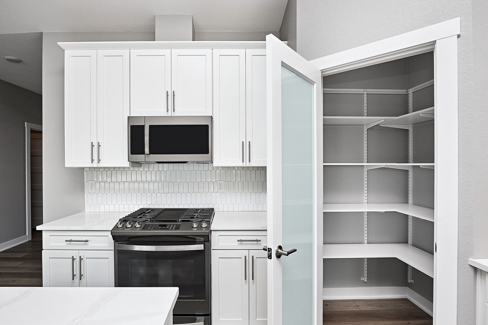 White kitchen with stove, microwave, and open pantry closet with empty shelves