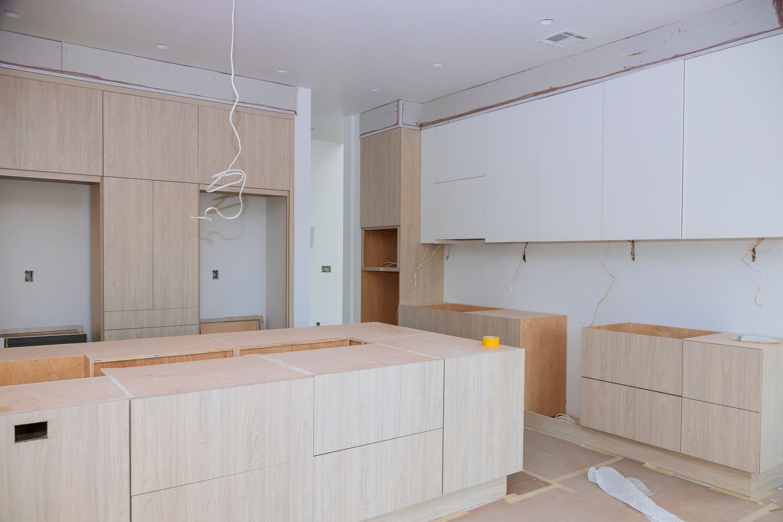 Unfinished kitchen with light wood cabinets and white upper cabinets in a bright room