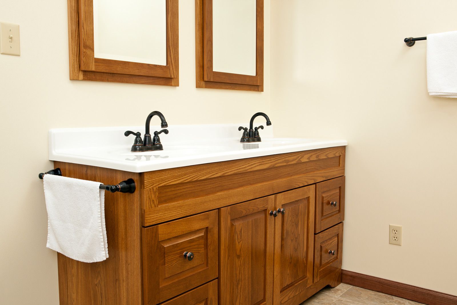 Wooden double vanity with white sink top and black faucets in a beige bathroom