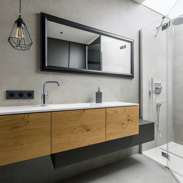 Modern bathroom with floating wood vanity, black-framed mirror, sink, and glass shower enclosure