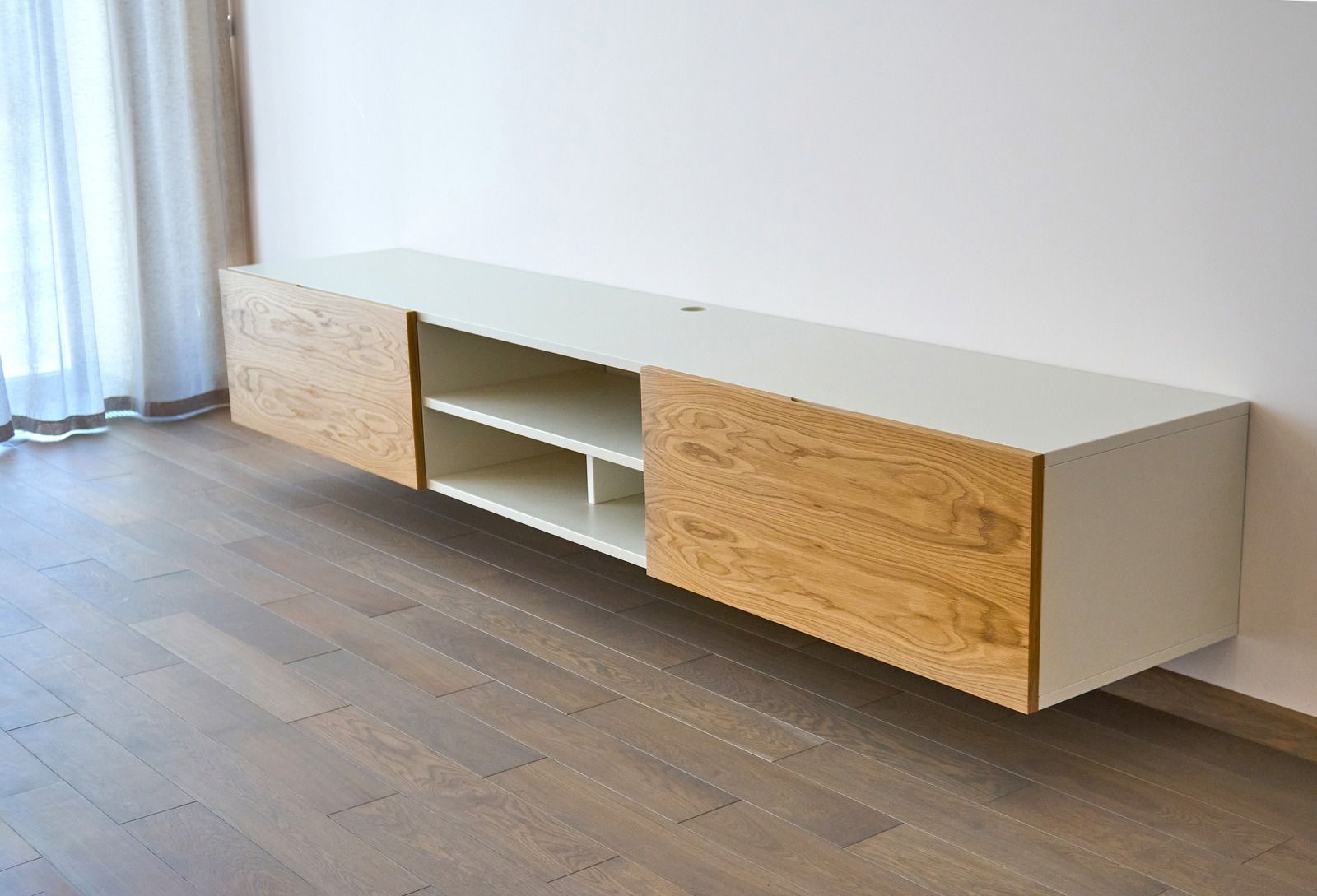 Modern low wooden media console with open shelves against a wall in a bright room