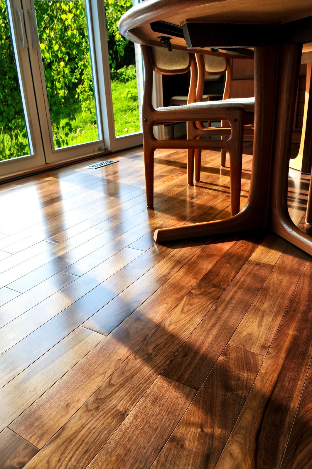 Sunlit wooden floor with table and chairs by a window overlooking greenery