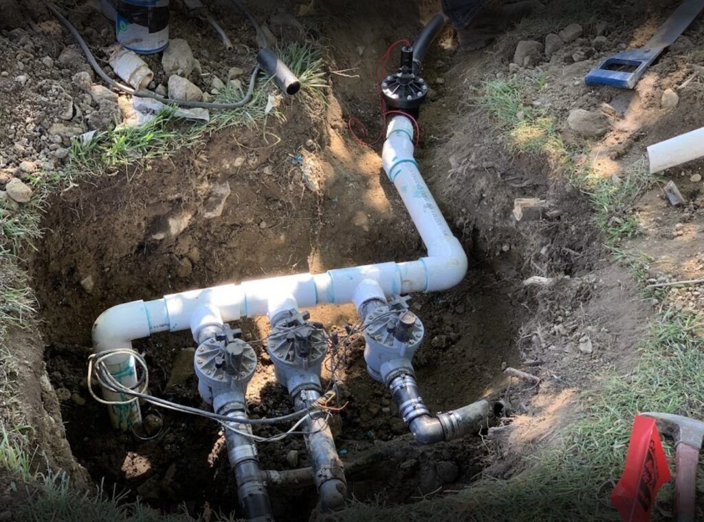 Exposed underground PVC plumbing manifold with pipes and valves in a dug trench