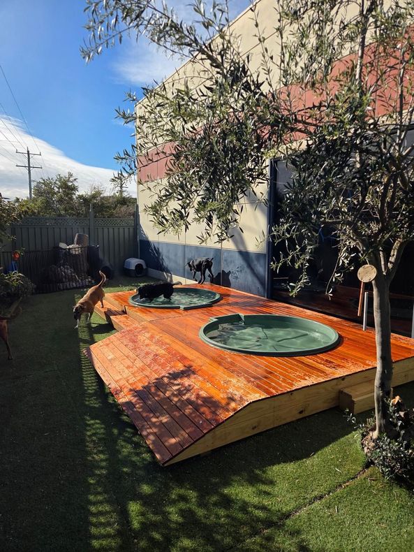 Backyard Wooden Hot Tub Deck With Two Round Tubs, Surrounded by Grass and a Fence — Pams Dog Day Club In Moolap, VIC
