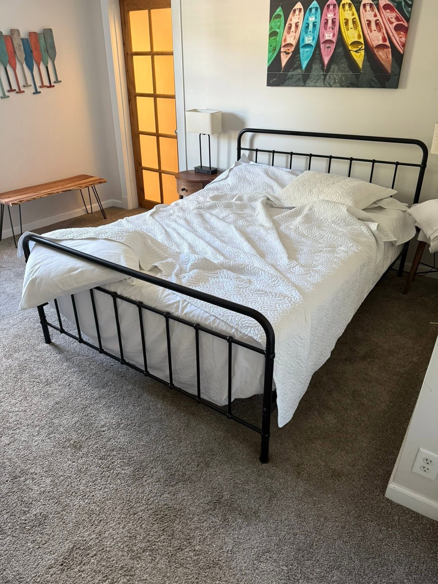Black metal bed with white bedding in a carpeted bedroom with wall art and a bench.