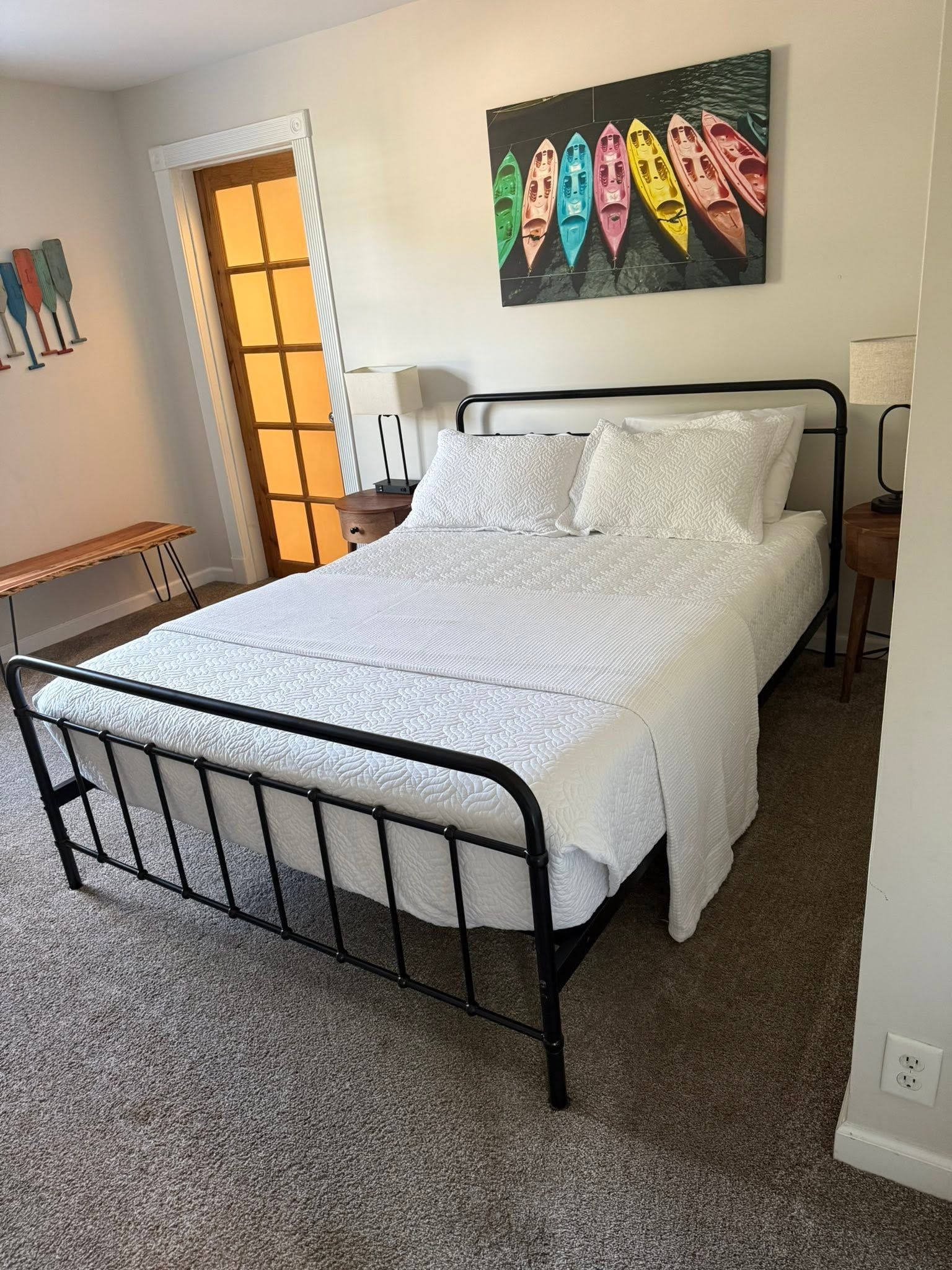 Bedroom with black metal bed, white bedding, colorful wall art, and carpeted floor.