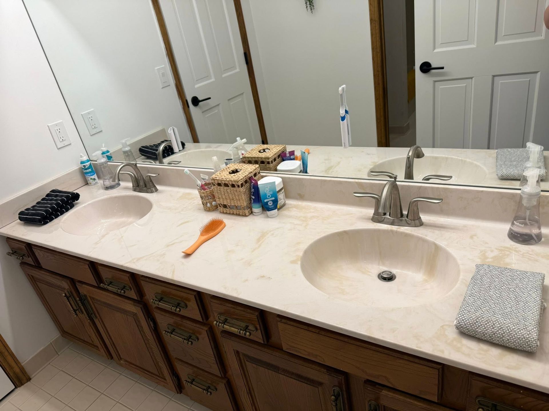 Bathroom vanity with two sinks, mirrors, toiletries, and a towel on the counter