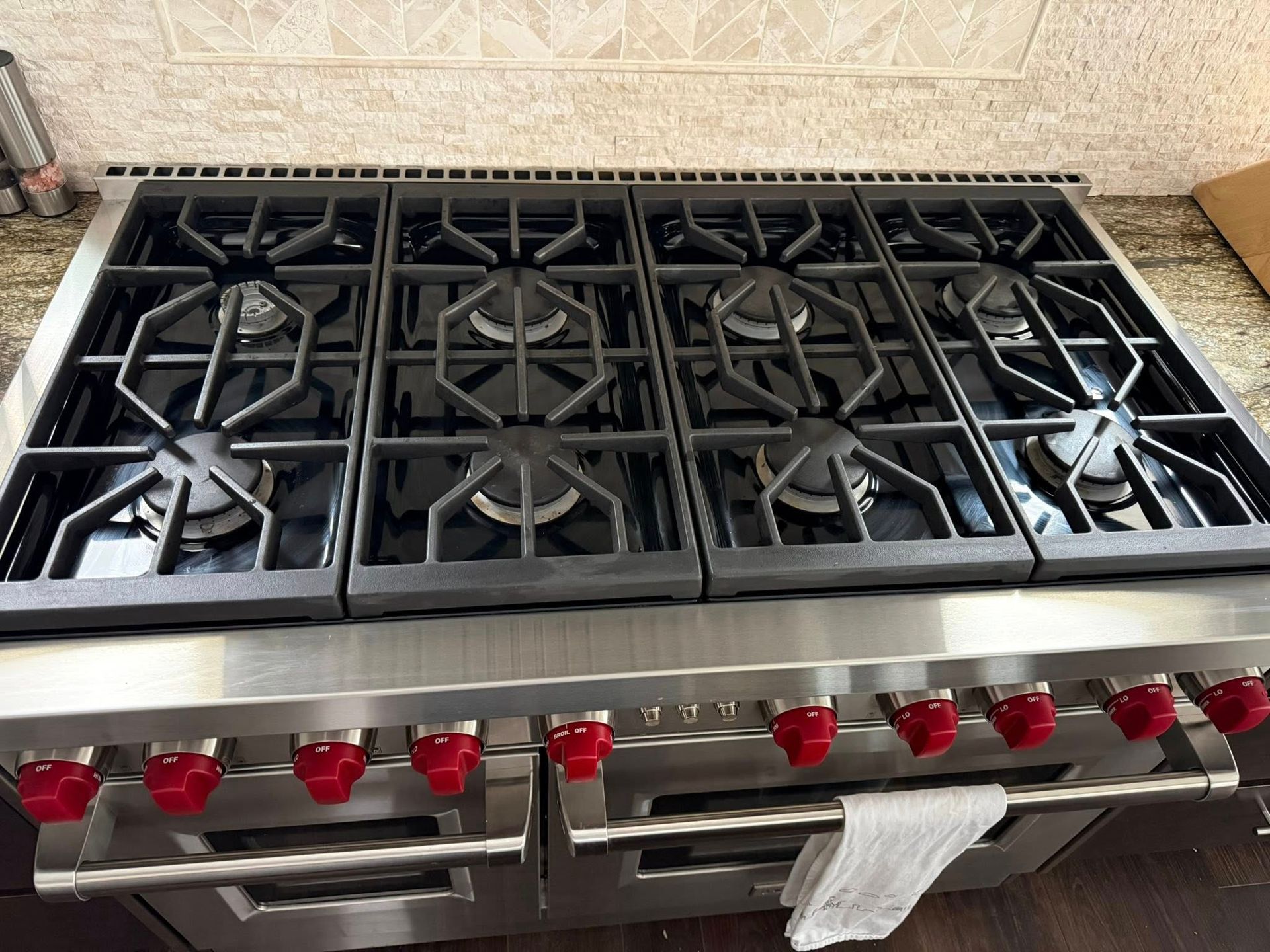 Stainless steel gas range with six black grates and red control knobs on a kitchen counter.
