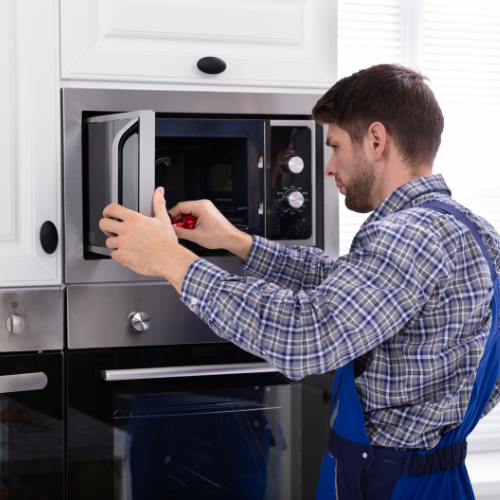 A man is fixing a microwave oven in a kitchen.