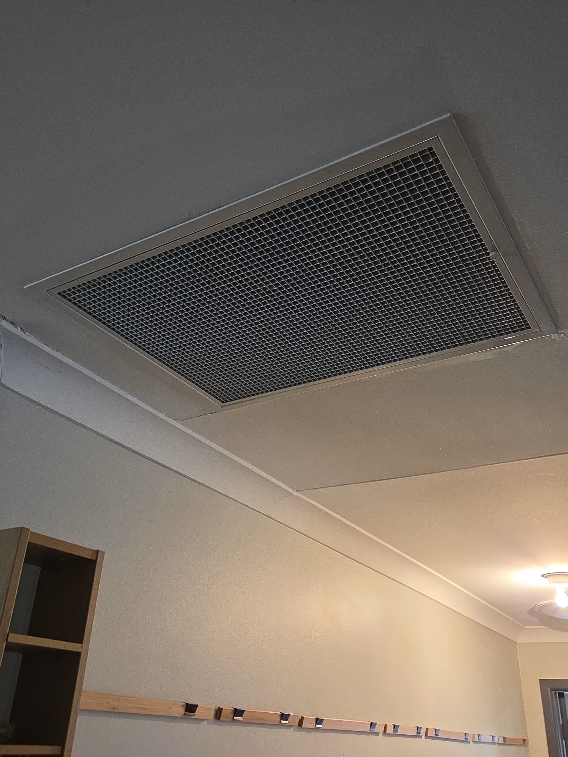 Ceiling with a large rectangular ventilation grille in a beige room, with a light fixture on the right. Ceiling with a large rectangular ventilation grille in a beige room, with a light fixture on the right.