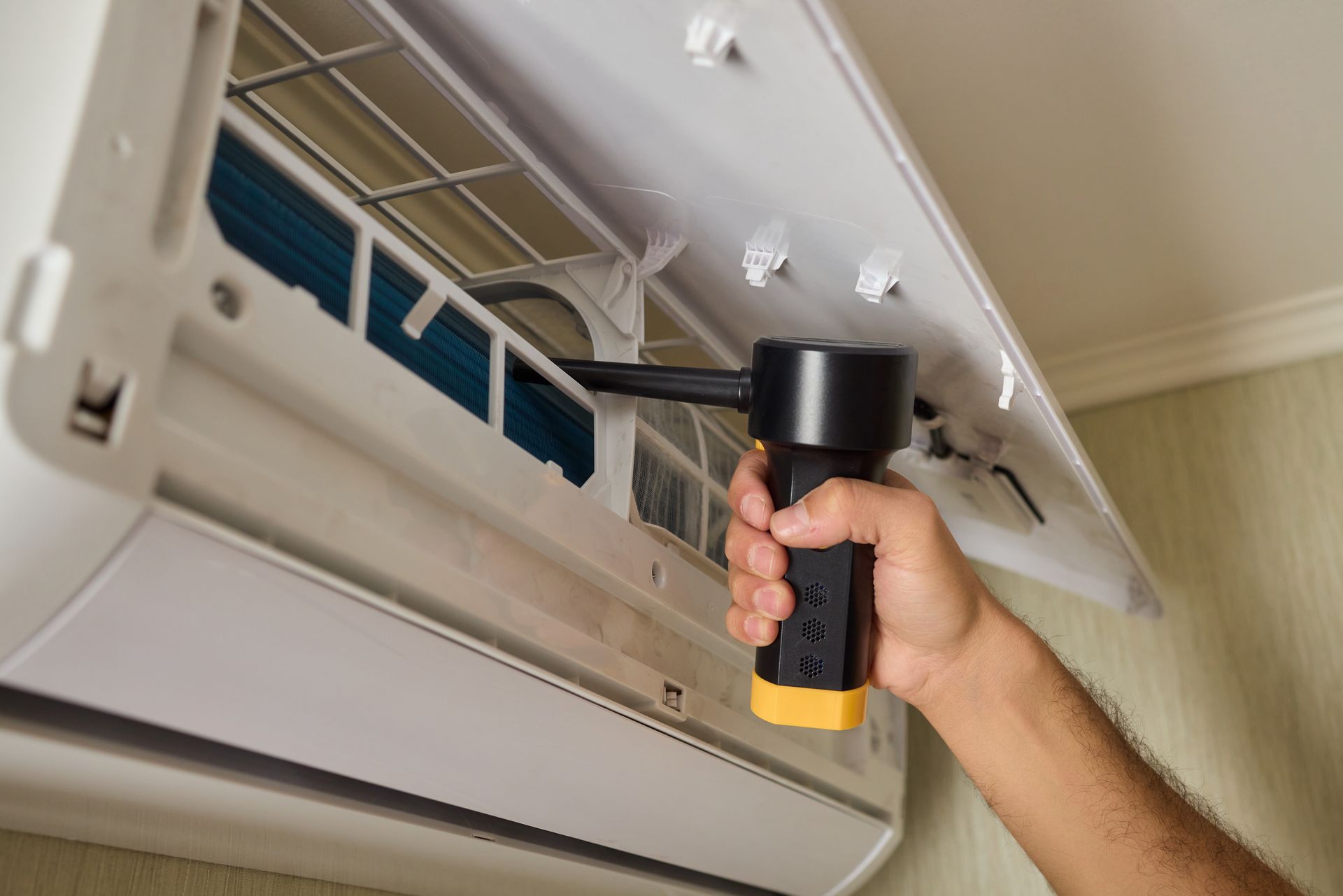 Hand cleaning a wall-mounted air conditioner filter with a handheld vacuum Hand cleaning a wall-mounted air conditioner filter with a handheld vacuum