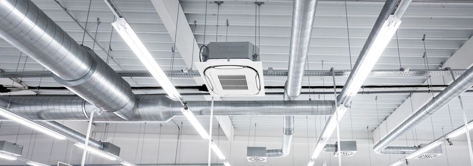 Ceiling of an industrial space with exposed ductwork, vents, and bright overhead lights