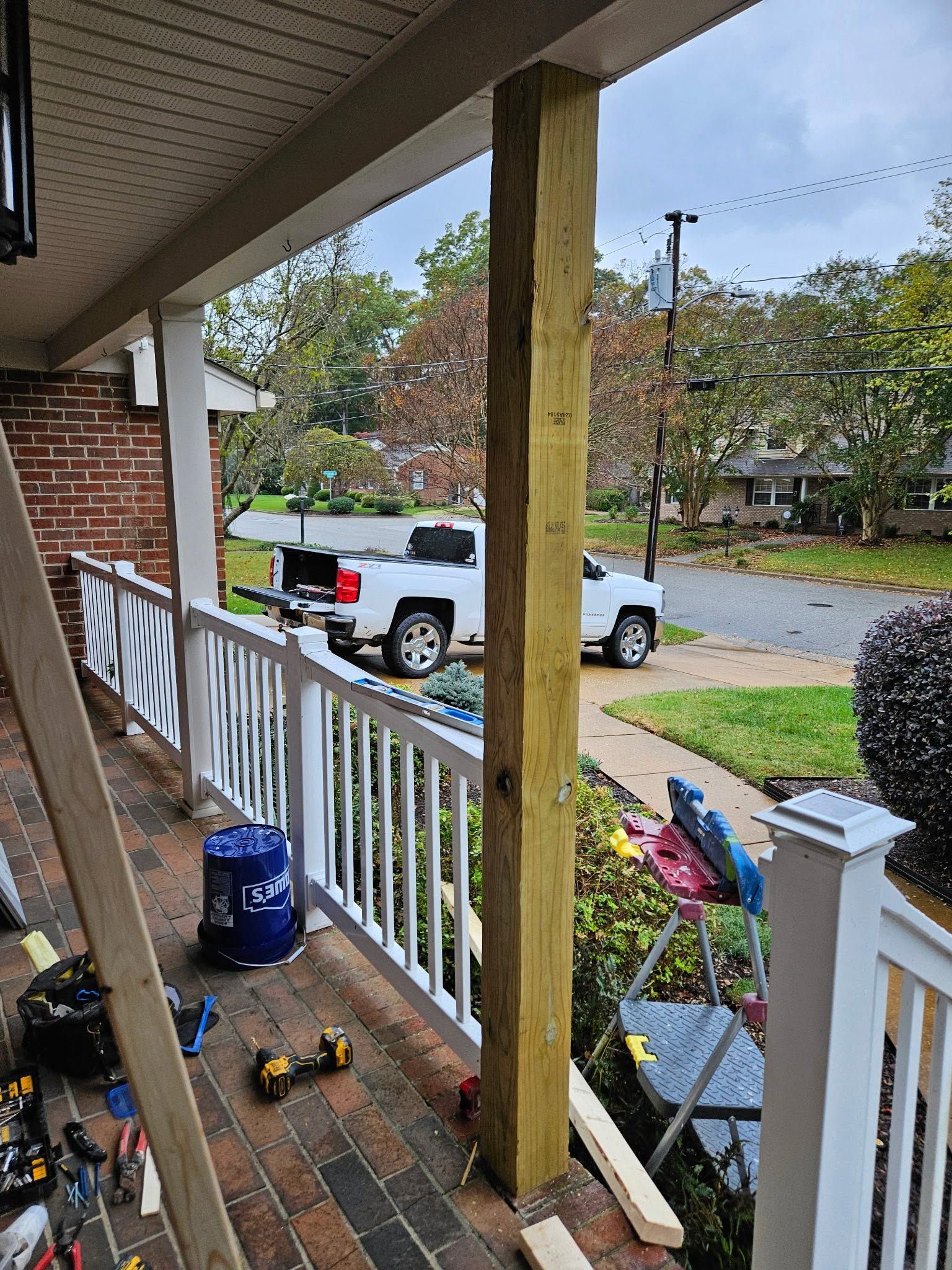 Front porch with a broken railing post, scattered tools, and a white pickup truck parked on the street.