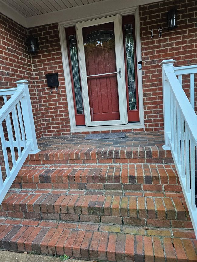 Brick front porch with red door, white railings, and wet steps leading up to the entrance