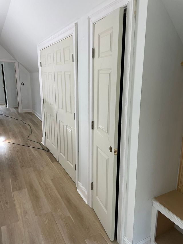 Hallway with white paneled closet doors and light wood flooring along a slanted wall