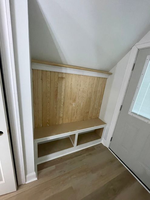 Built-in alcove bench with white shelves and wood paneling beneath a sloped ceiling.