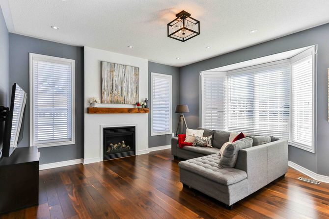 A painted grey living room with a couch and a white floor to ceiling living fireplace and wooden floors