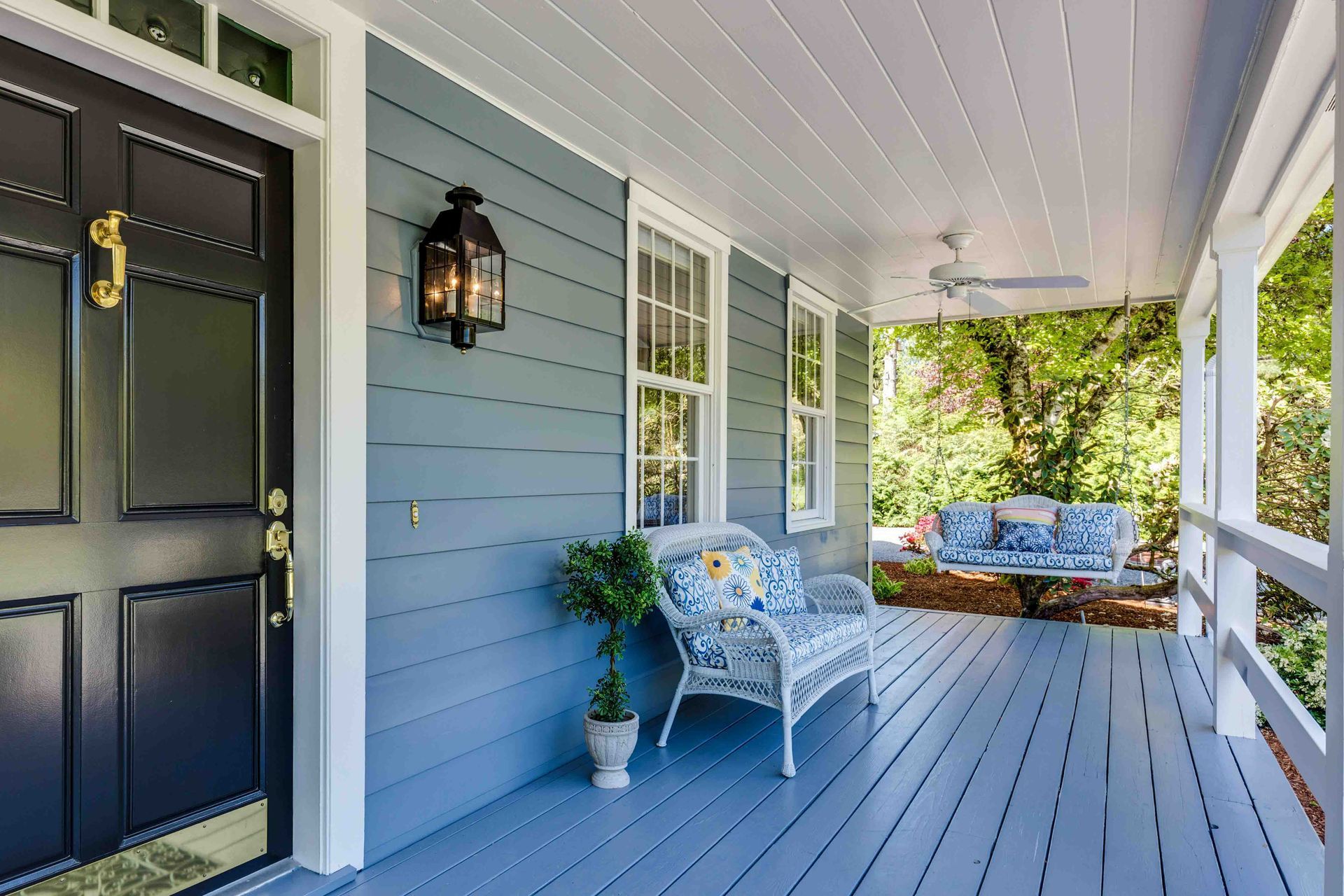 Freshly painted blue siding on a house on a front porch with a white ceiling and blue wooden floor. 