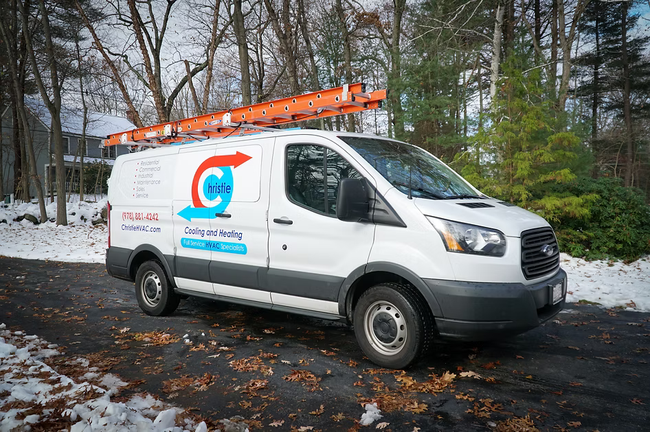 White service van with ladder, logo on side, parked on snowy road.