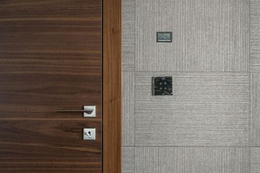 Wooden door with silver handle and keyhole, next to patterned wall with a small display and keypad.