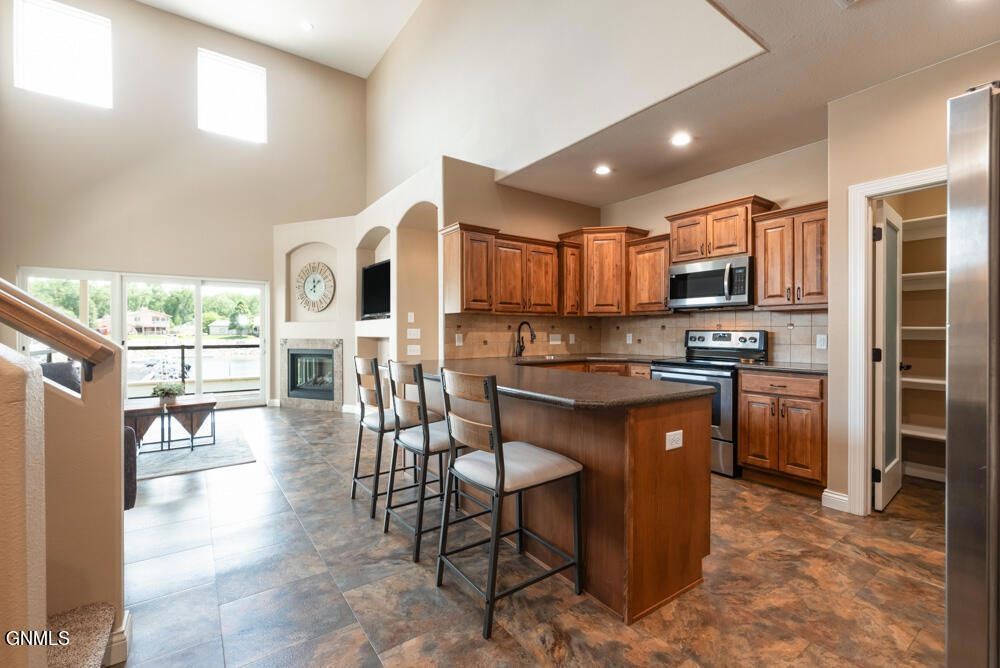 A kitchen with wood cabinets, a center island with two bar stools, a fireplace, and a walk-in pantry.