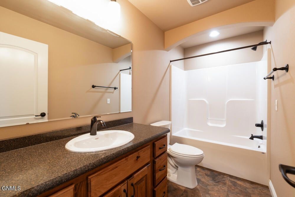 A bathroom with a dark-topped wooden vanity, a large mirror, and a white bathtub-shower combo with black hardware.