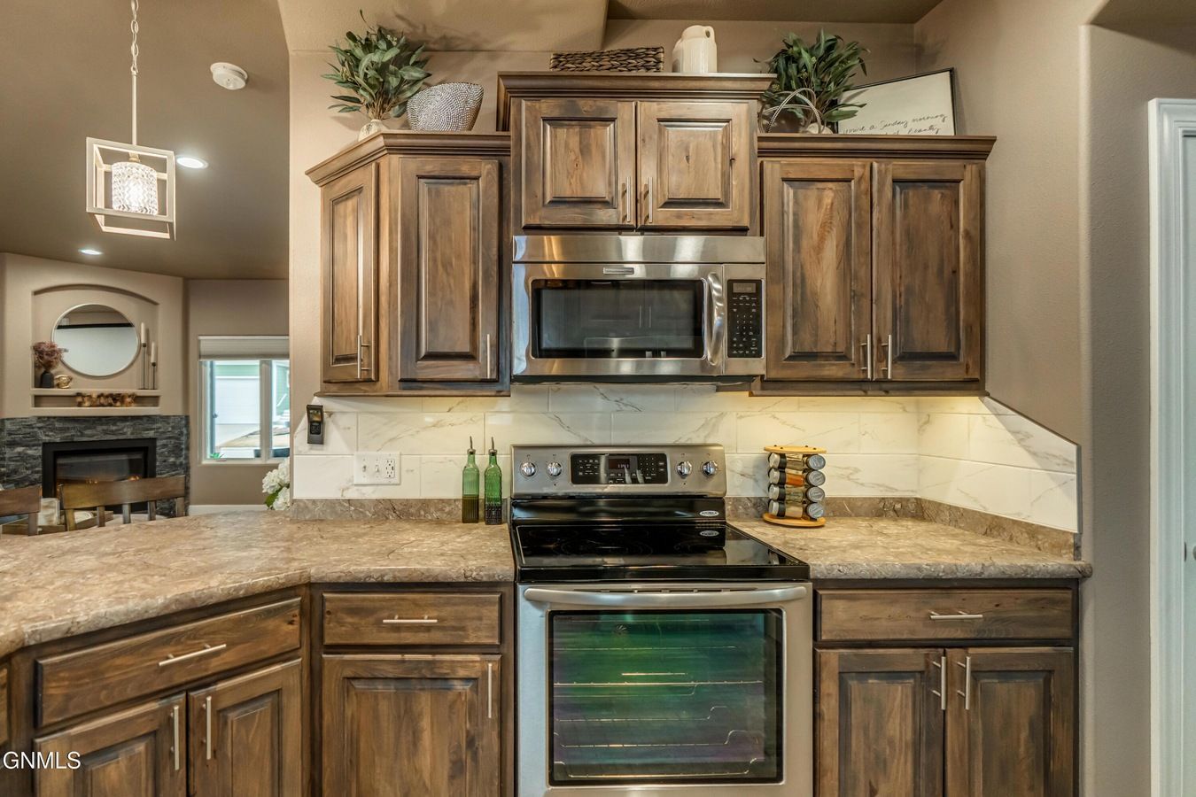A rustic kitchen with dark wood cabinets, a stainless steel microwave and oven, stone countertops, and under-cabinet lights.