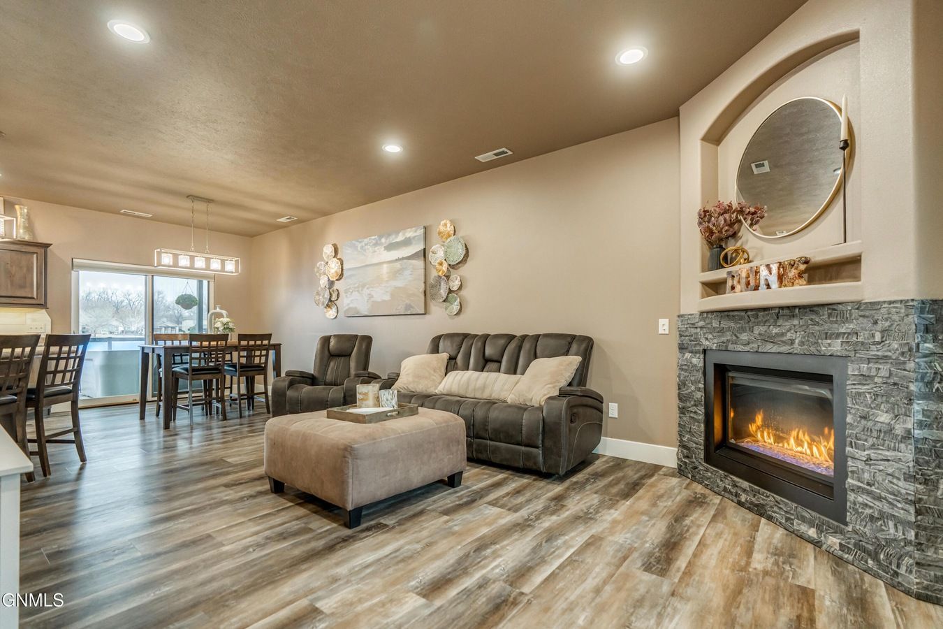 A furnished open-concept living and dining area featuring a stone fireplace, a gray sectional sofa, and wood flooring.