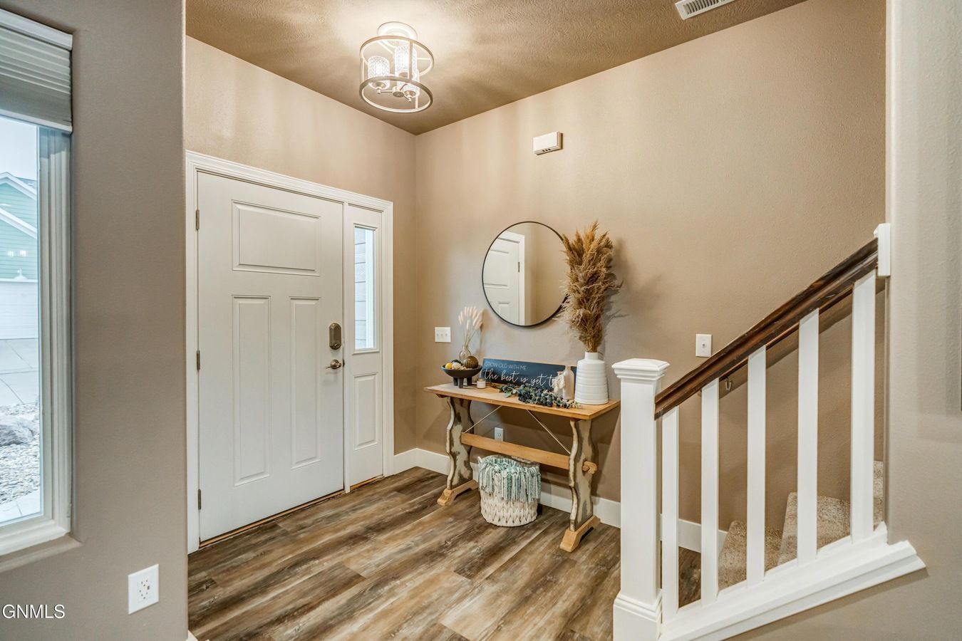 An entryway with wood floors, a white door with a side window, a console table with a mirror, and a staircase.