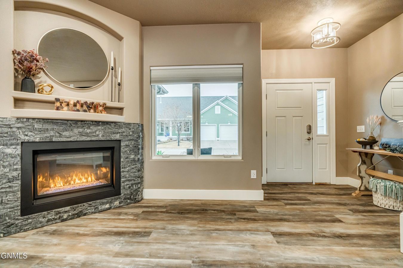 A neutral-toned room featuring a stone-faced fireplace with an oval mirror, a window, and a white front door.