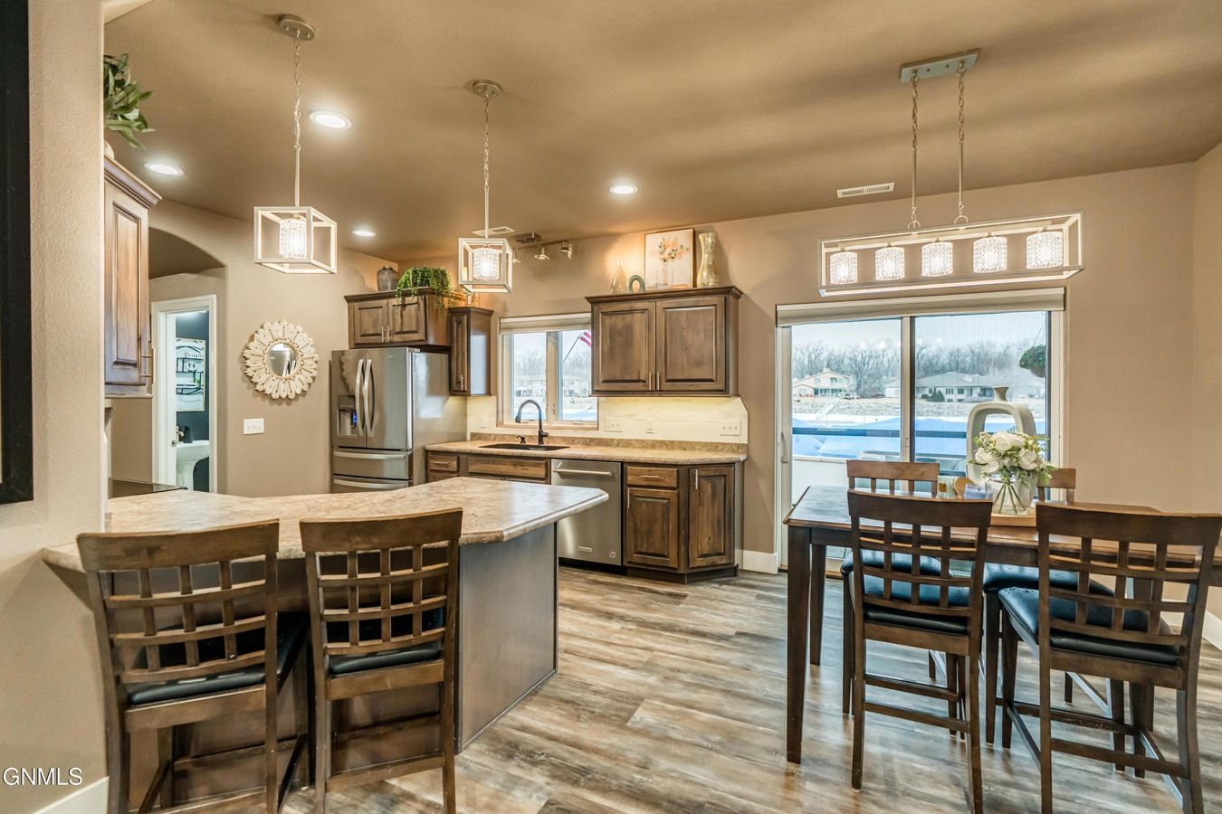A kitchen with wood cabinets, stainless appliances, a central island with bar seating, and a dining table by a patio door.