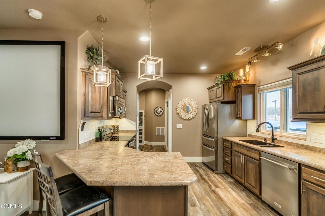 Modern kitchen with tan countertops, dark wood cabinets, stainless steel appliances, and two pendant lights overhead.