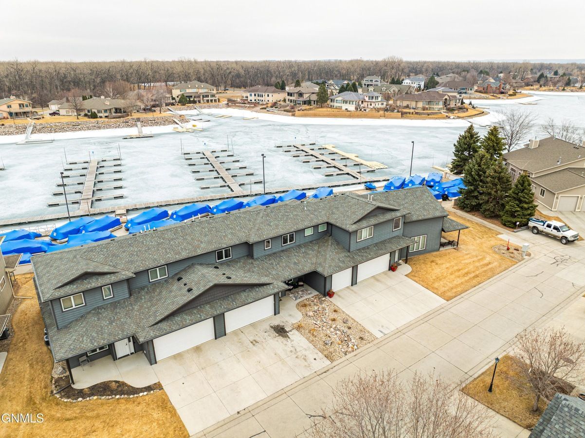Aerial view of a gray, multi-unit building with a marina featuring docks and boats covered in blue tarps on a frozen lake.