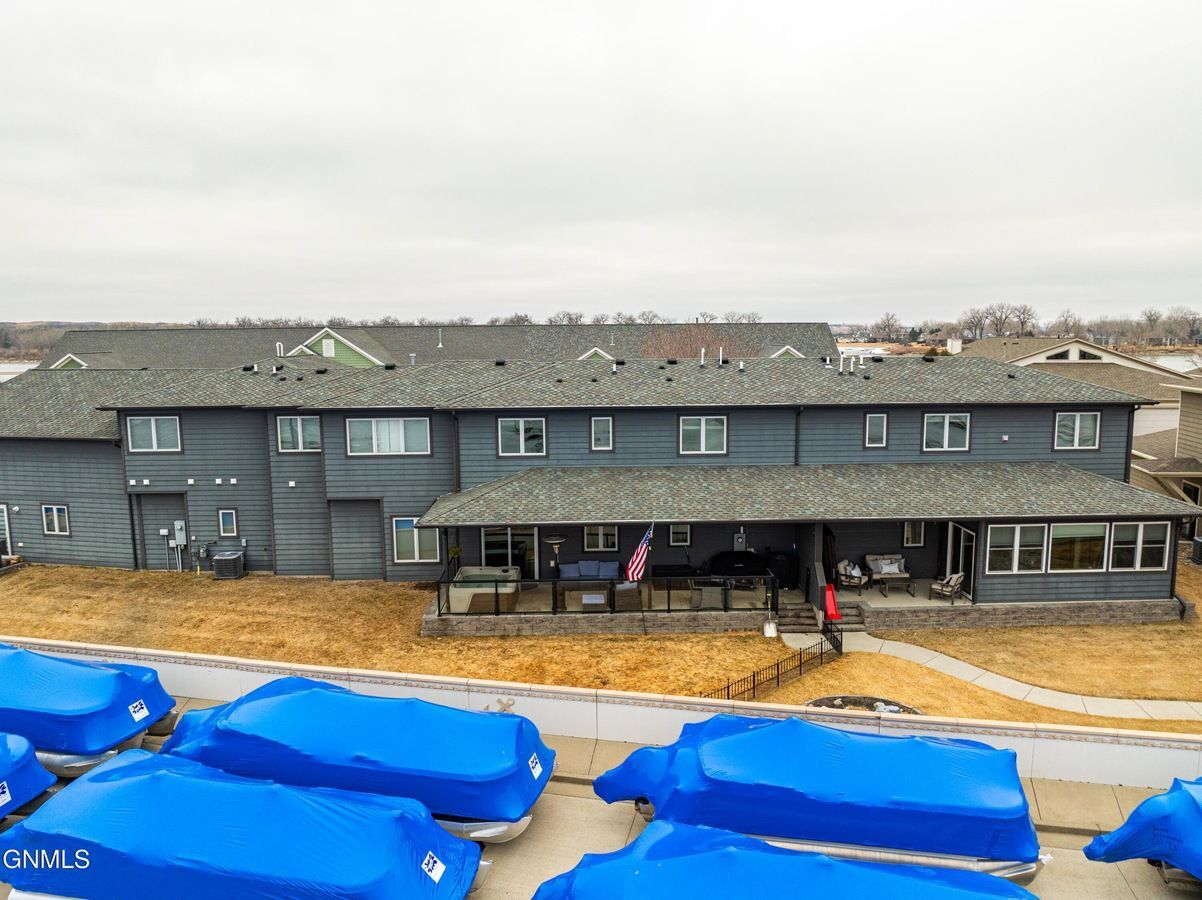 A gray multi-unit building with a covered patio, set behind several rows of boats covered in blue tarps.