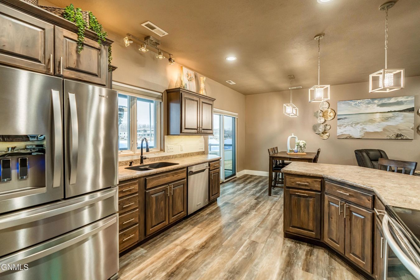A modern, open-concept kitchen with stainless steel appliances, dark wood cabinetry, light countertops, and a dining area.
