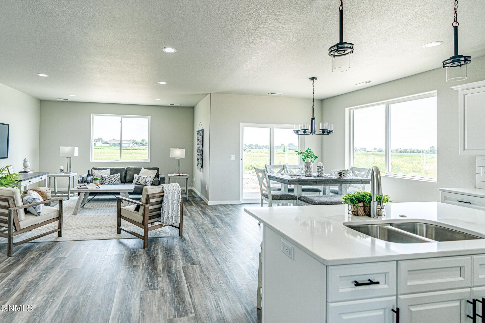 A bright, open-concept living and dining area with wood floors, neutral walls, contemporary lighting, and large windows.