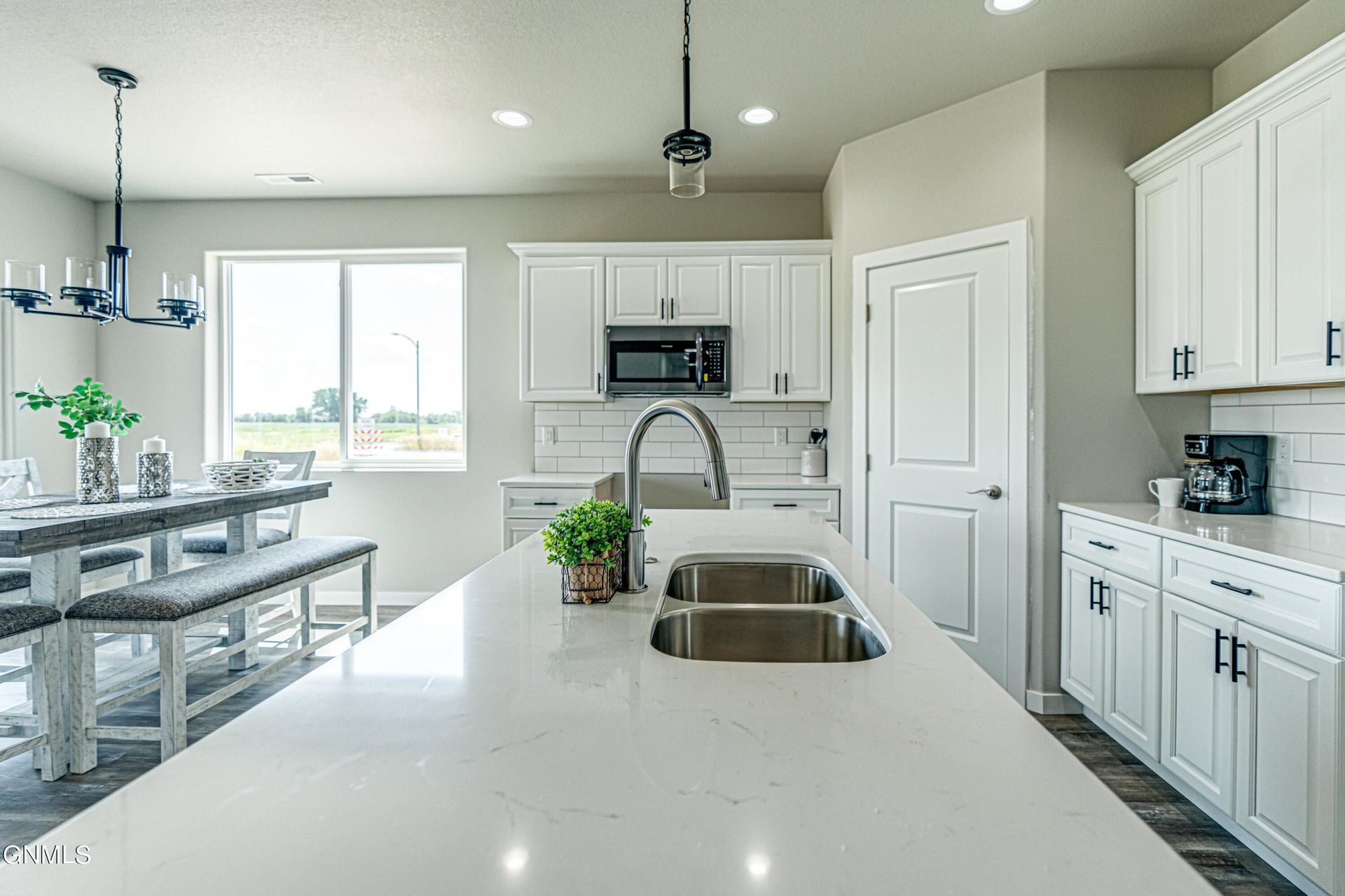 A bright, modern kitchen featuring white cabinets, a large quartz island with a double sink, and a dining area with benches.