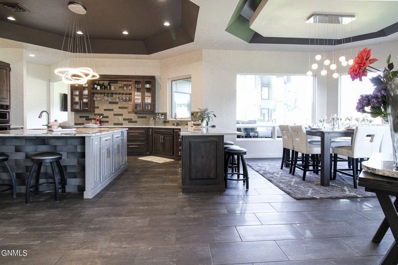 Modern, open-concept kitchen and dining area featuring dark tile floors, white cabinets, and two kitchen islands.